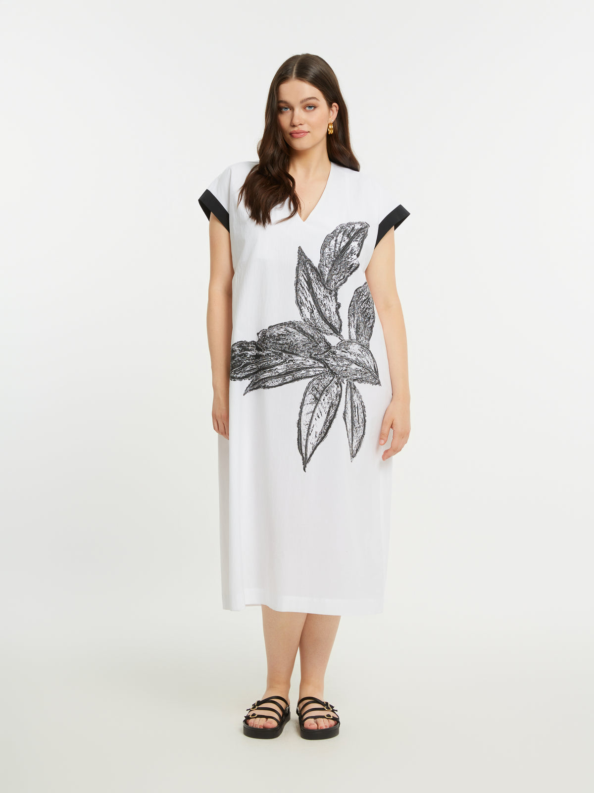 Woman wearing a white dress with black floral design on a plain background