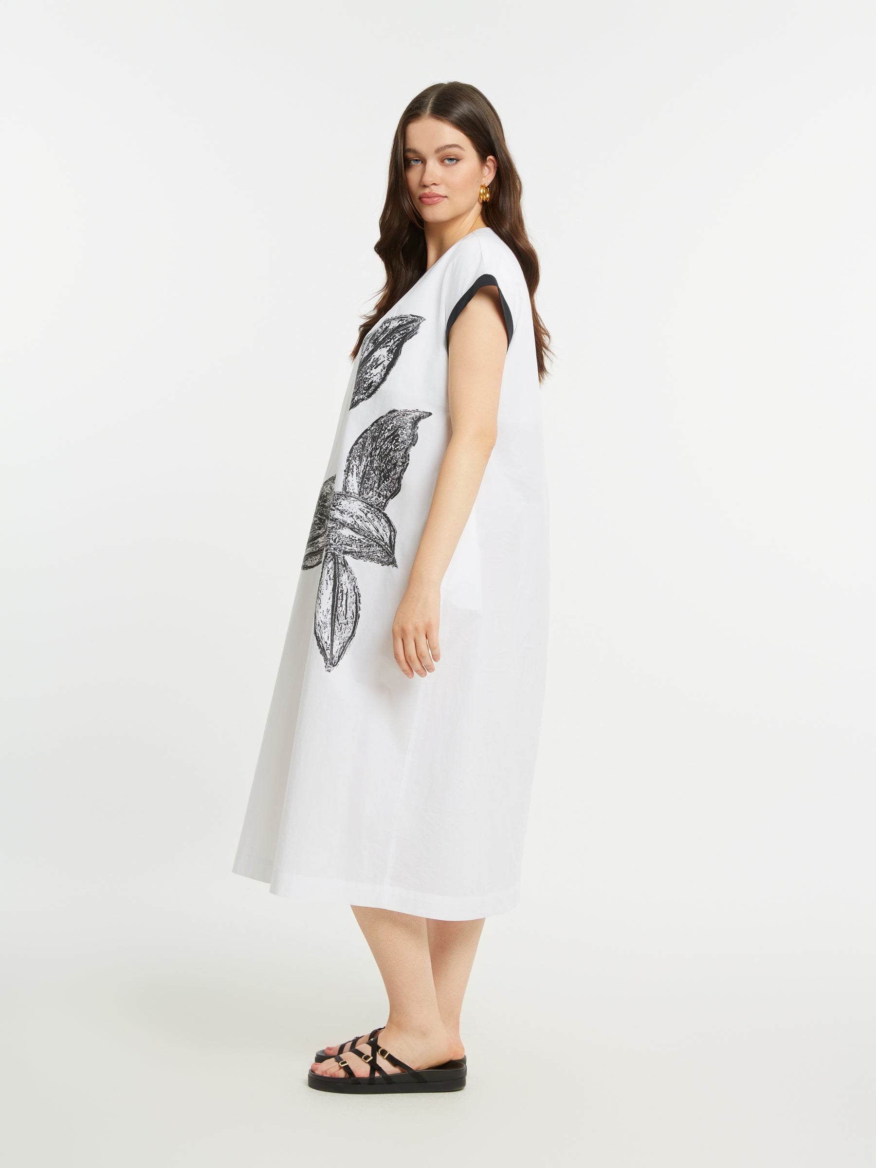 Woman wearing a white dress with a black floral design on a plain background