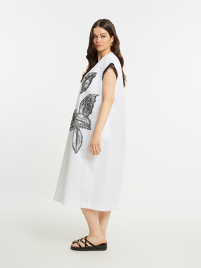 Woman wearing a white dress with a black floral design on a plain background