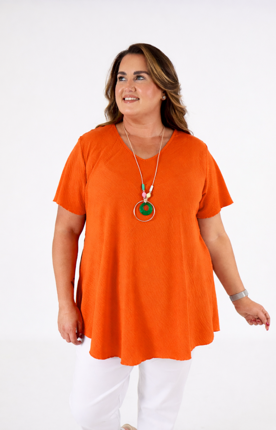 Woman wearing an orange top and white pants on a white background