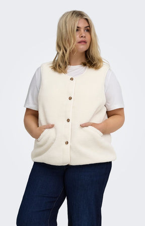 A woman modeling the Only Carmakoma Baby Gilet in Cream, a cream-colored, sleeveless fuzzy button-up vest over a white t-shirt and dark blue jeans, set against a plain light gray background.