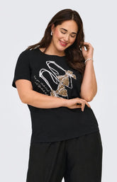 A woman modeling the Only Carmakoma Beau T-Shirt in Black,  a black short-sleeve t-shirt with a graphic of a high-heeled shoe in leopard print and white trim, paired with black pants, against a light gray background. This image was created using AI.