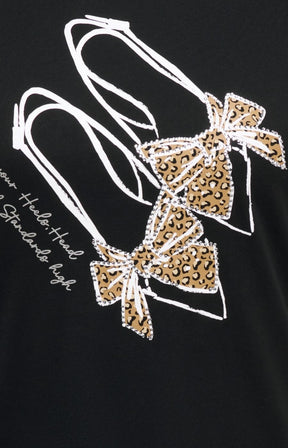 Close-up of the Only Carmakoma Beau T-Shirt in Black, a black t-shirt featuring a graphic print of two high heels decorated with leopard print bows and white outline details, alongside white script text. This image was created using AI.