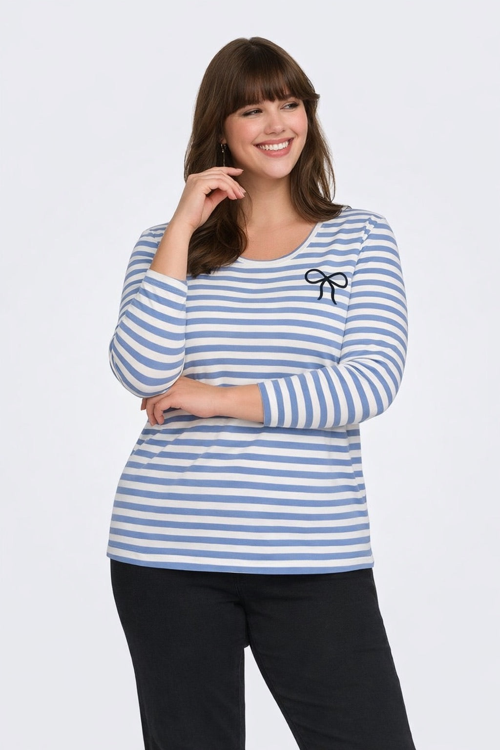 Woman wearing a blue and white striped long-sleeve top with a small bow detail on the chest, standing against a white background.
