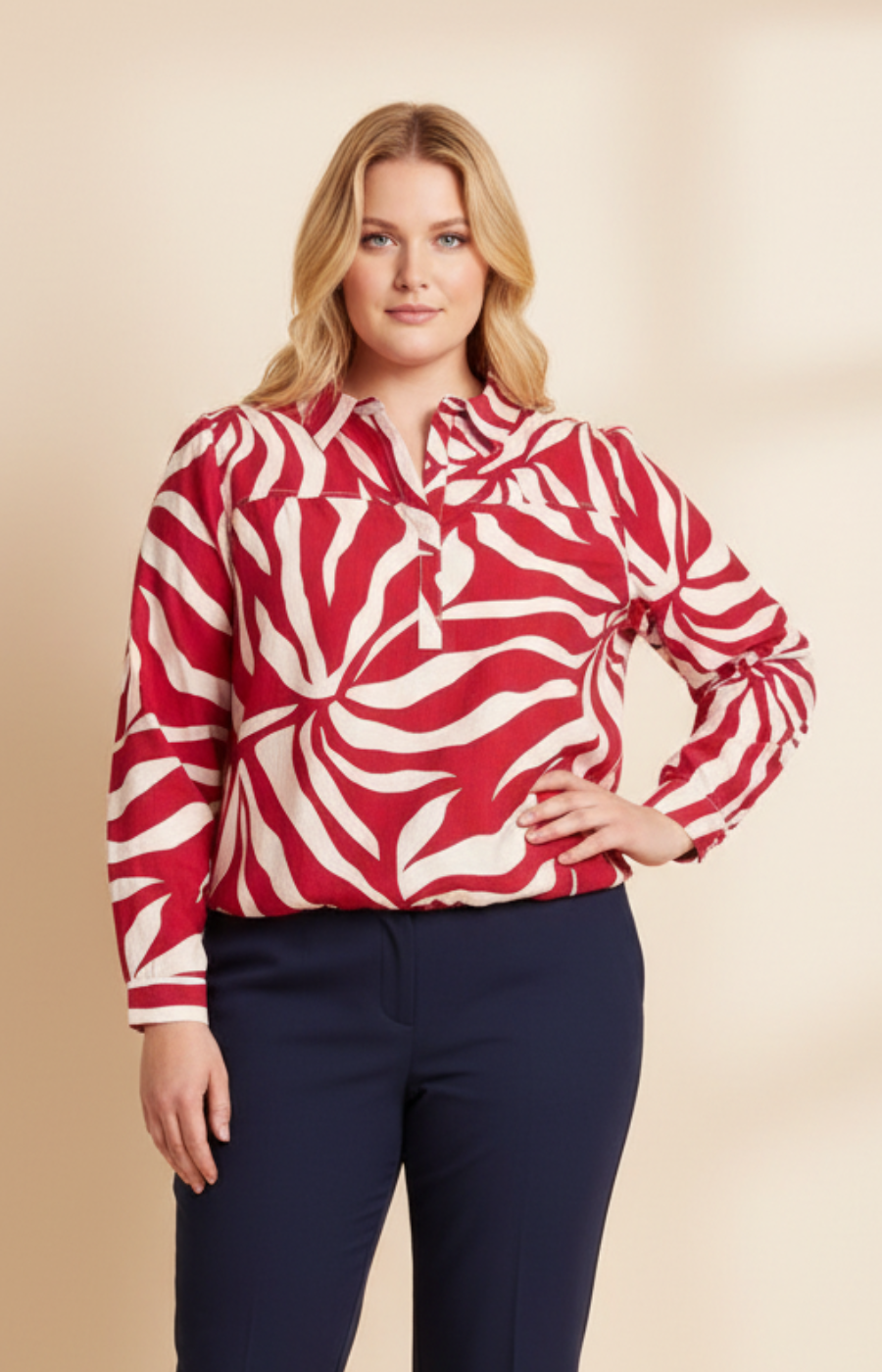 Woman wearing a red and white patterned blouse with navy pants on a beige background