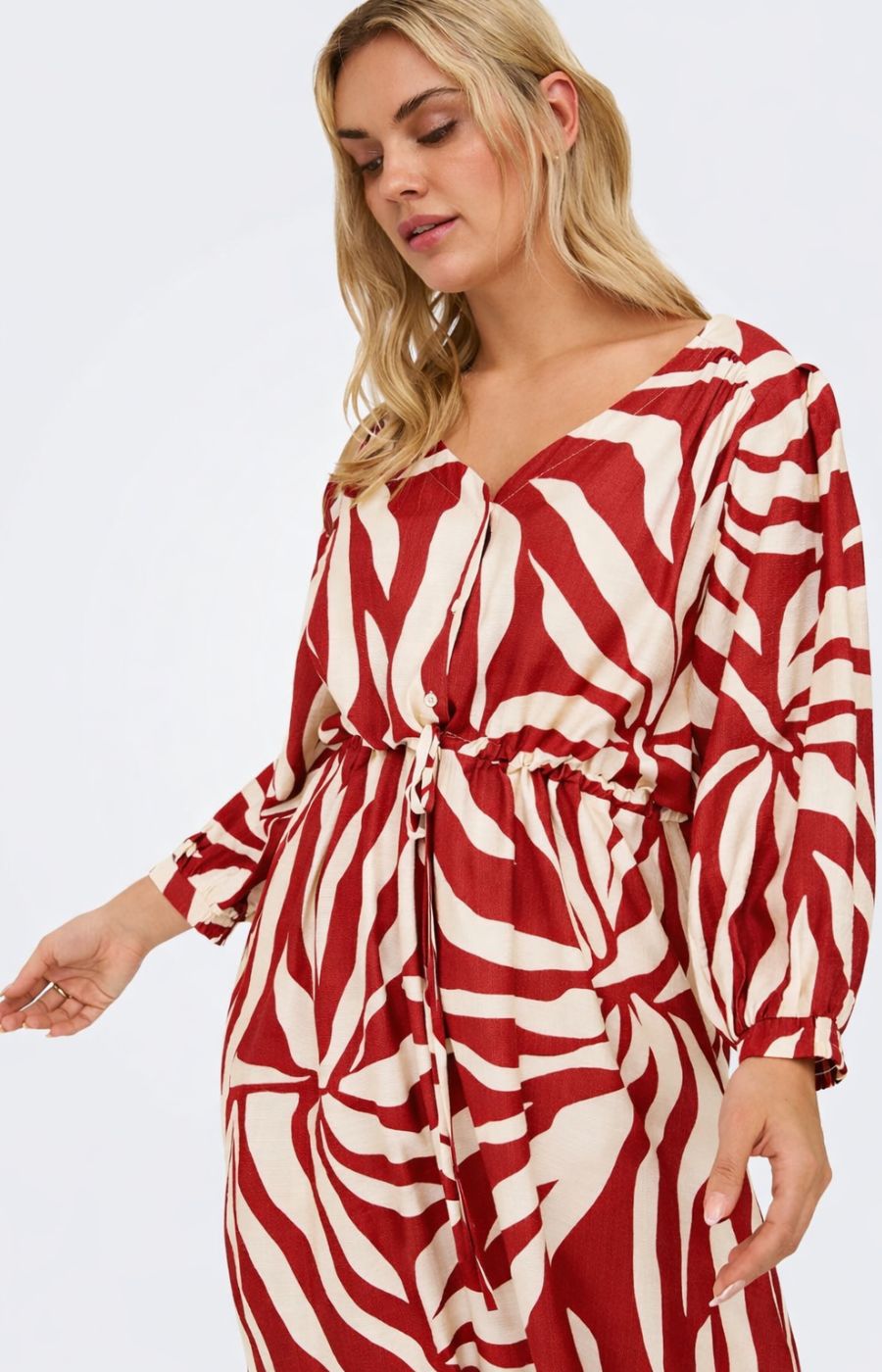 Woman wearing the Only Carmakoma Camille Dress in Red, a red and white patterned dress with a V neckline leading to a short button placket, long cuffed sleeves, a tiebelt in the waist and has a midi length, on a plain background