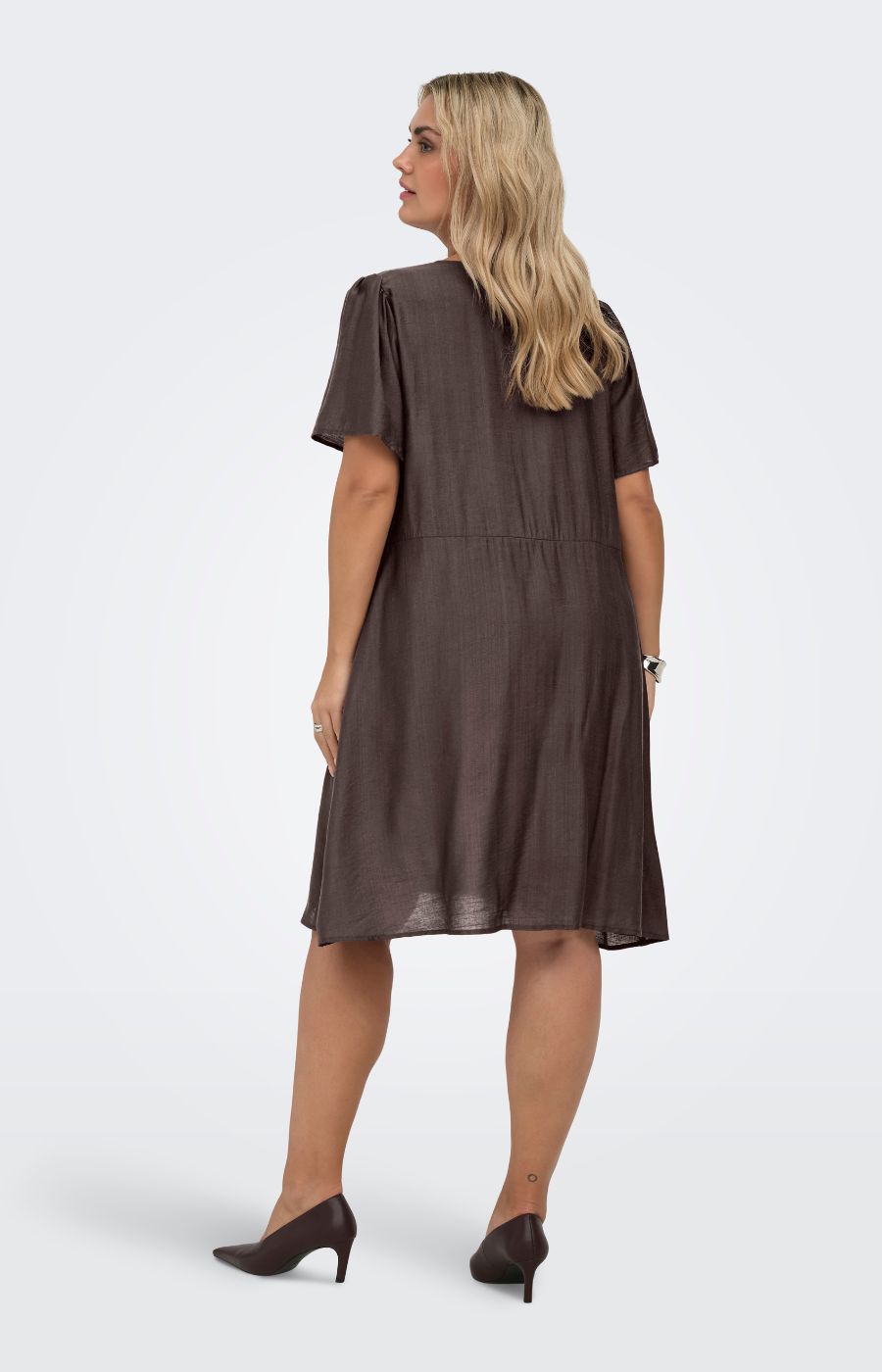 Woman wearing the Only Carmakoma Cecilia Dress in Brown, a brown dress on a white background