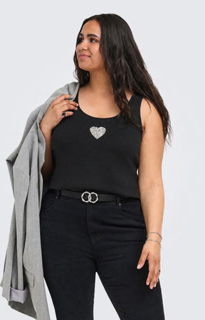 A woman modeling the Only Carmakoma Iris Vest Top in Black, a black sleeveless tank top with a sparkling silver heart emblem on the chest, paired with black jeans and a gray blazer draped over her shoulder, against a light gray background. This image was created using AI.
