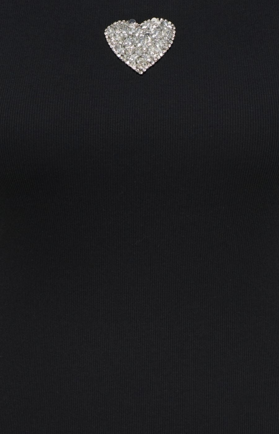 A close-up of the Only Carmakoma Iris Vest Top in Black, a black ribbed knit garment featuring a small, heart-shaped silver rhinestone heart near the neckline.