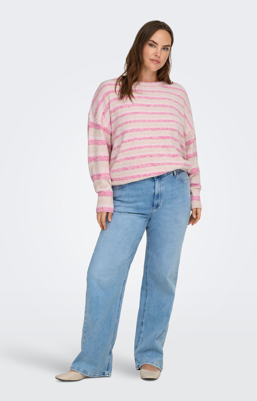 Woman wearing Only Carmakoma Johanna Knit in Pink, a pink and white striped sweater and blue jeans on a white background