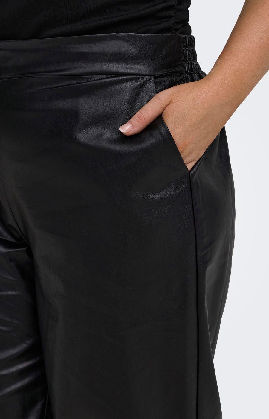 Close-up of a person wearing the Only Carmakoma Kari Trousers in Black, black straight leg trousers with a gathered elastic waistband and side pocket, shown against a light grey background.