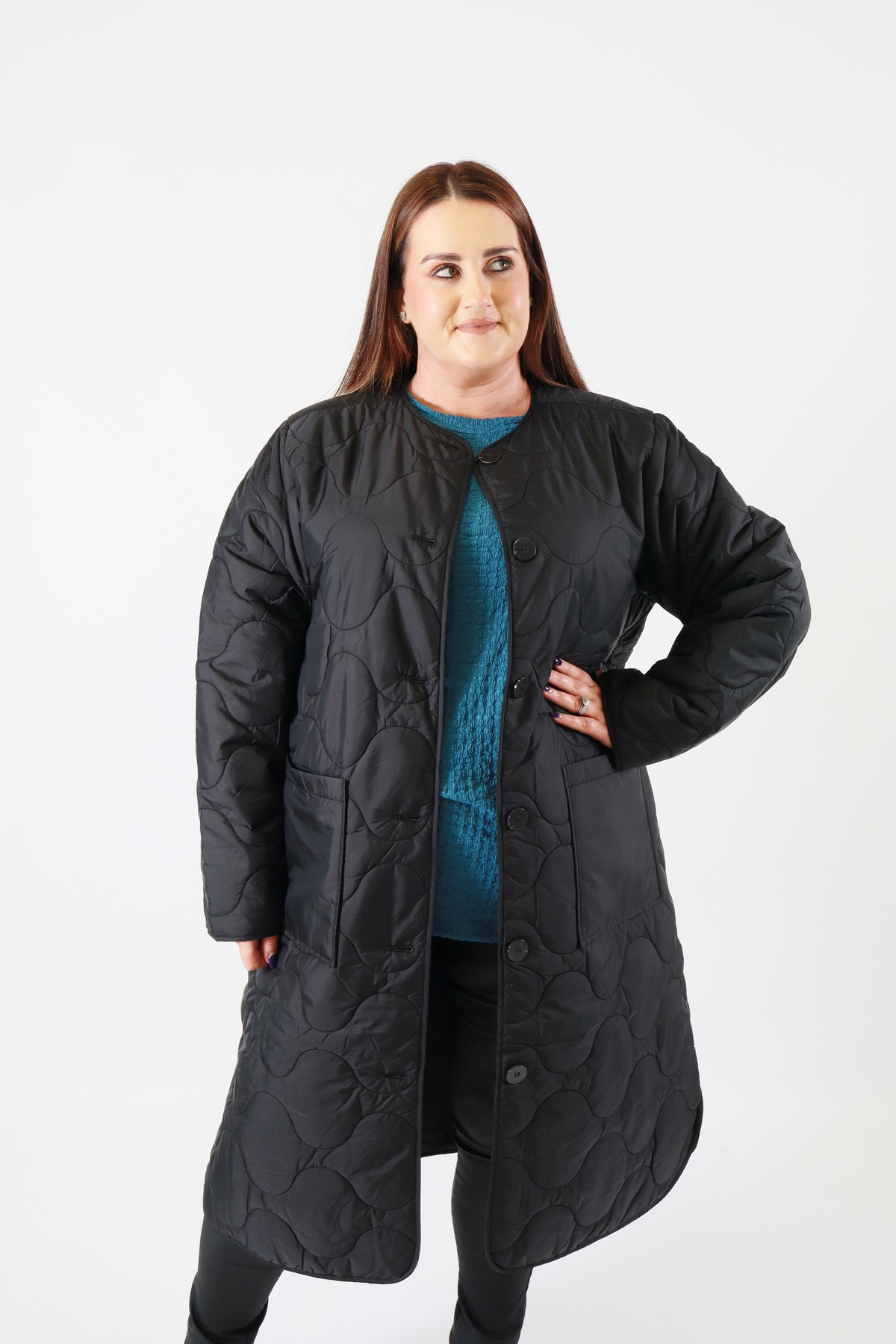 Person wearing a long black quilted coat on a white background