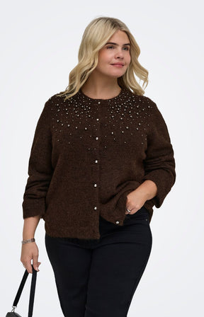 A woman modeling  the Only Carmakoma Miggie Cardigan in Coffee Bean, a dark brown knit cardigan sweater with silver rhinestone embellishments across the chest, paired with black pants against a plain white studio background.