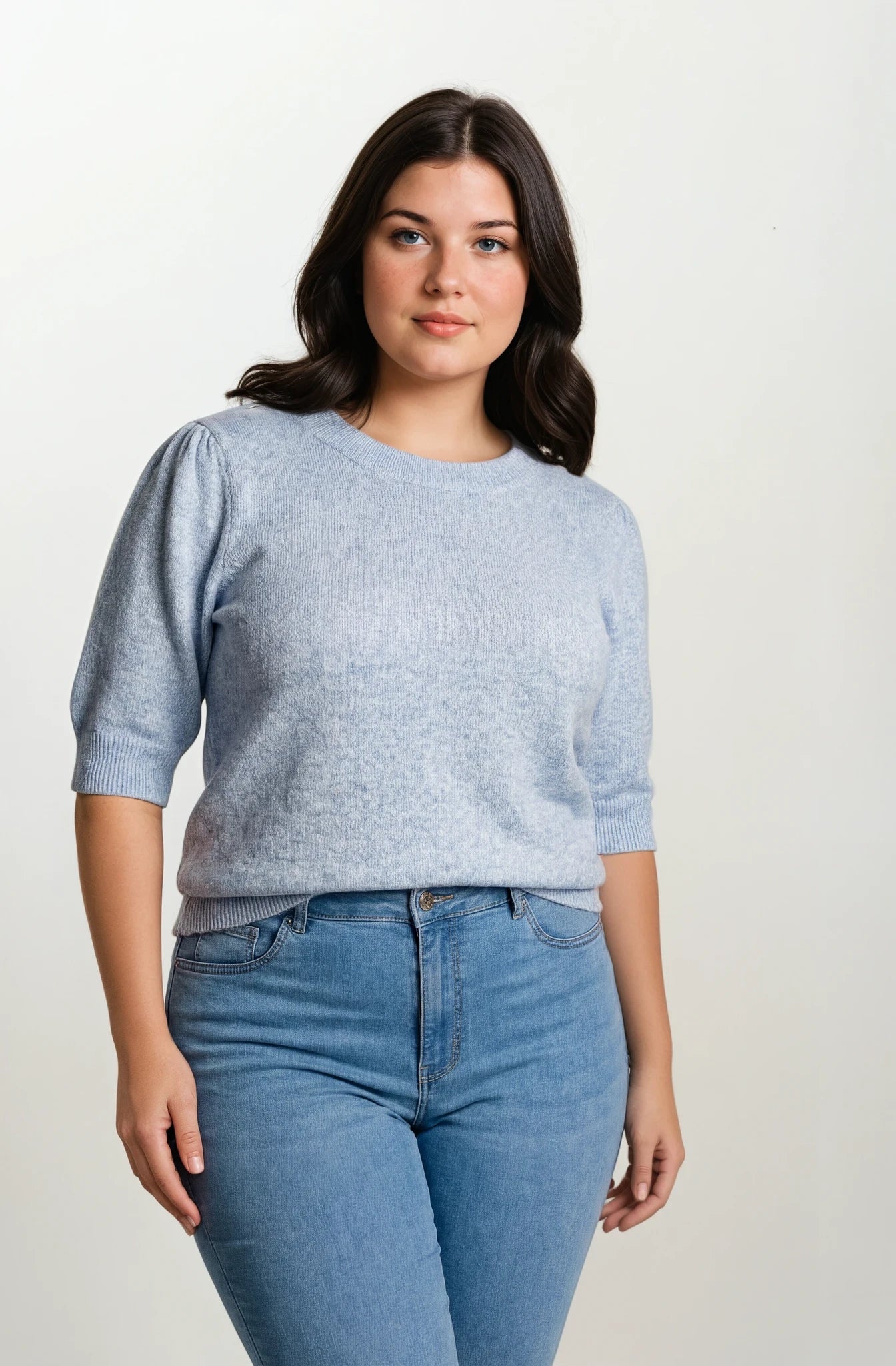 Front facing model wearing a light blue fine knit sweater and light blue jeans on a grey background.