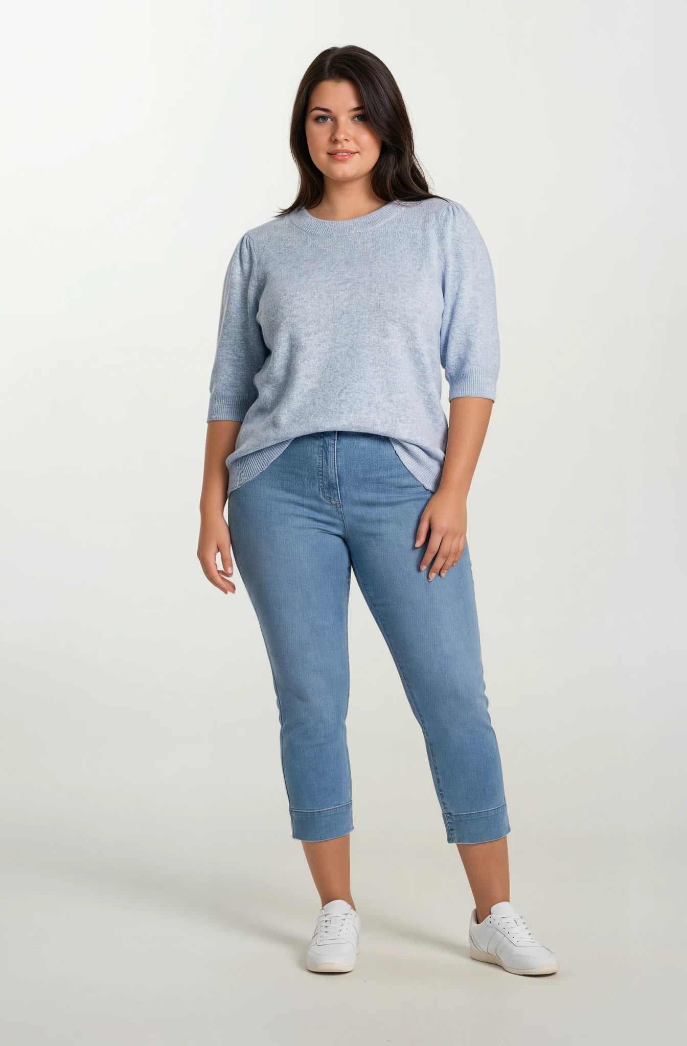 Woman wearing a light blue sweater and jeans on a white background