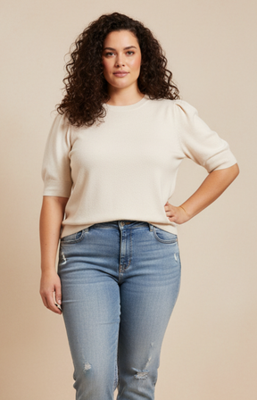Woman wearing a beige sweater and blue jeans against a beige background