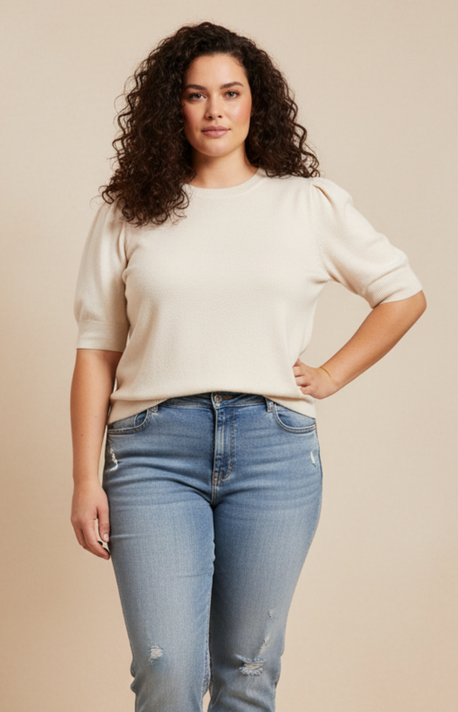 Woman wearing a beige sweater and blue jeans against a beige background