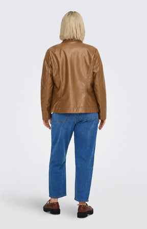 A woman modeling the Only Carmakoma Robber Faux Leather Jacket in Cognac, a cropped tan faux-leather jacket over a white top and blue jeans, standing against a light gray studio background. This image was created using AI.