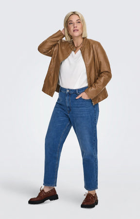A woman modeling the Only Carmakoma Robber Faux Leather Jacket in Cognac, a cropped tan faux-leather jacket over a white top and blue jeans, standing against a light gray studio background. This image was created using AI.