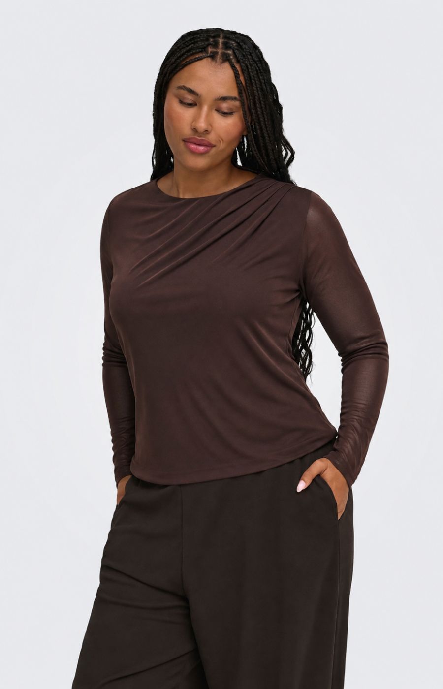 Model wearing the Only Carmakoma Sara Top in Chocolate, a round neck, long mesh sleeve top, with draping on the shoulder, worn with brown trousers, This image was created using AI. 