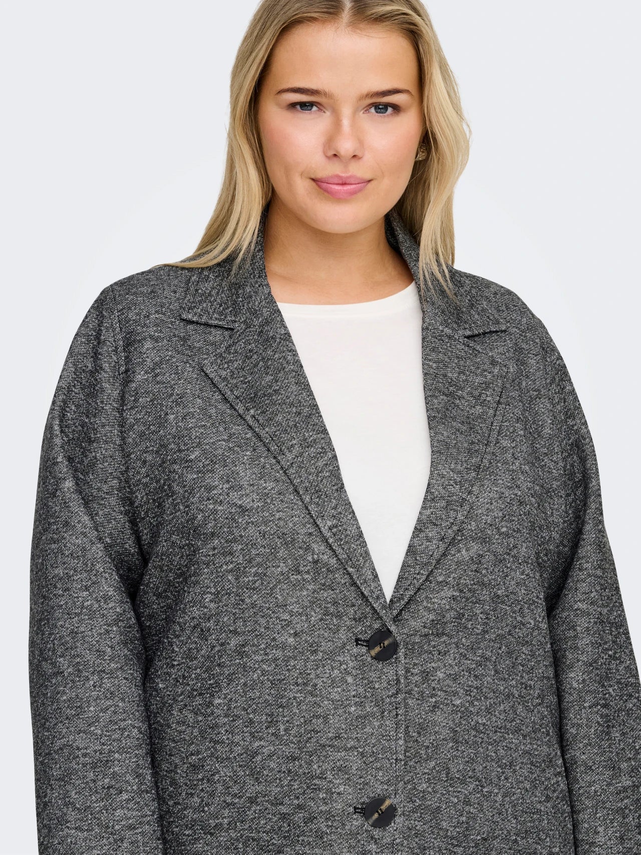 Woman wearing a gray coat over a white top on a plain background