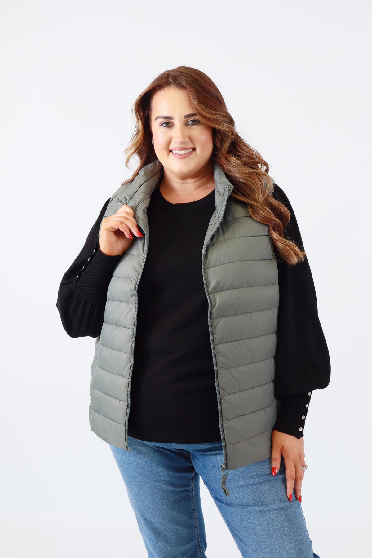 Woman wearing a gray puffer vest over a black top and blue jeans on a white background