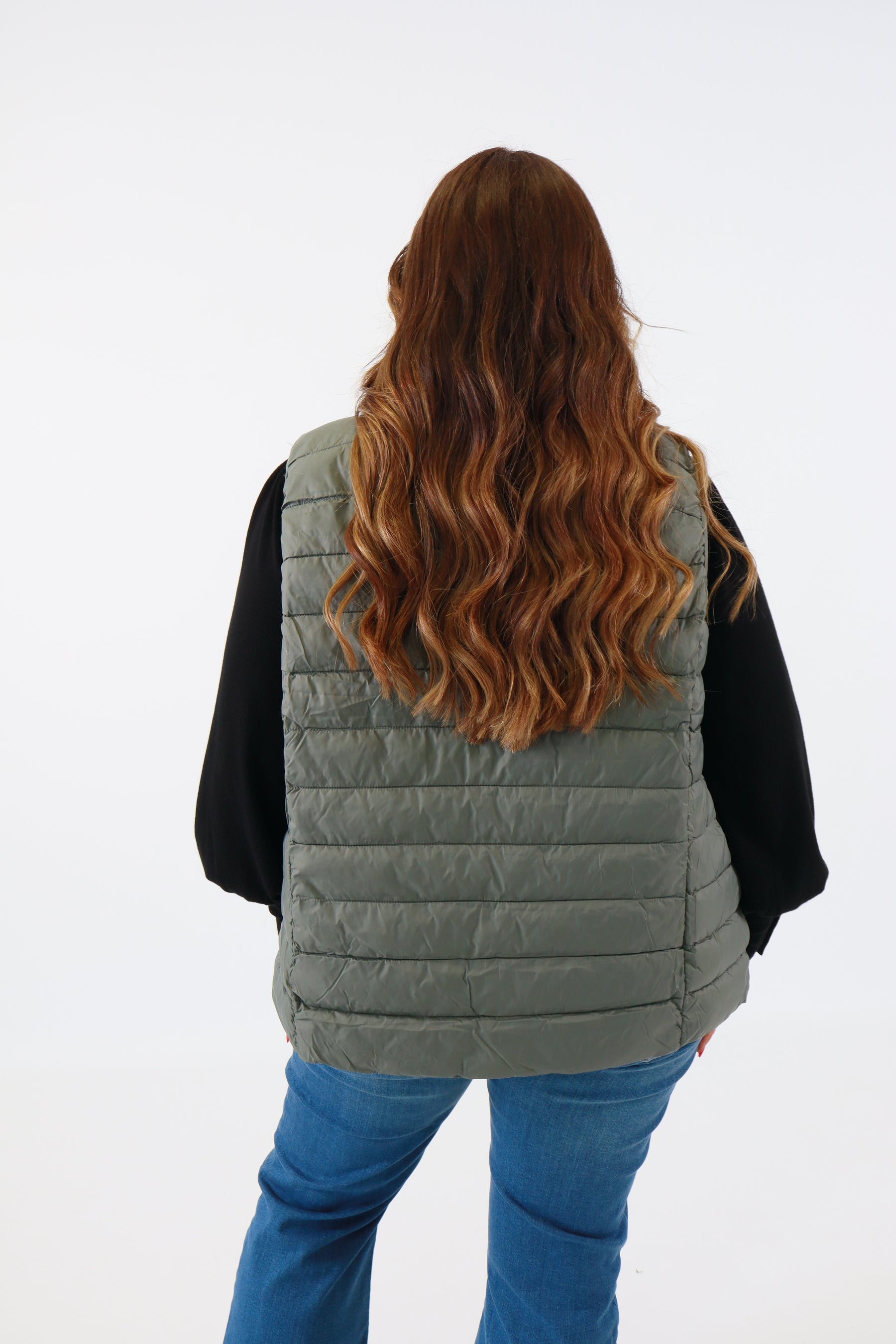 Person wearing a gray quilted vest with a white background