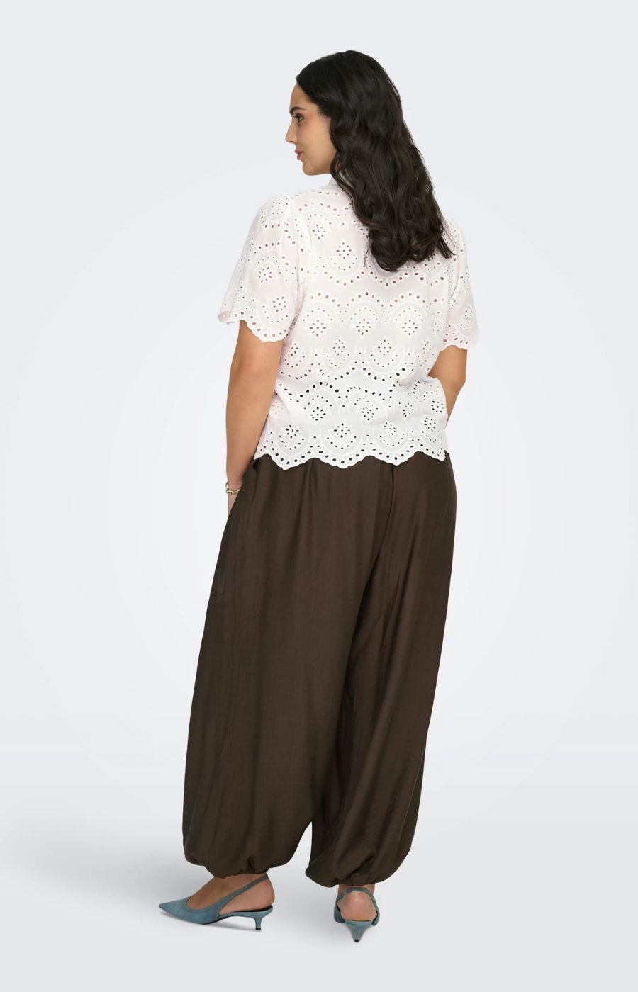 Woman wearing a white lace top and brown wide-leg pants on a white background