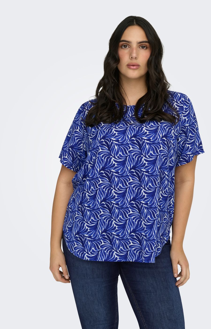 Woman wearing a blue patterned Vica top with dark denim jeans on a white background