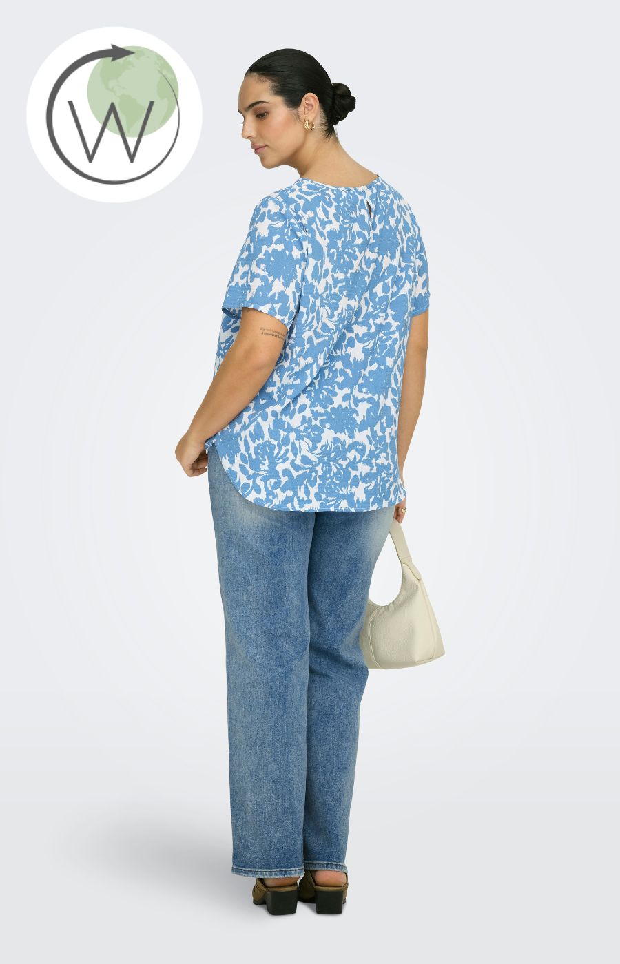 Woman wearing a blue and white floral patterned blouse and light wash jeans, holding a beige handbag on a light gray background