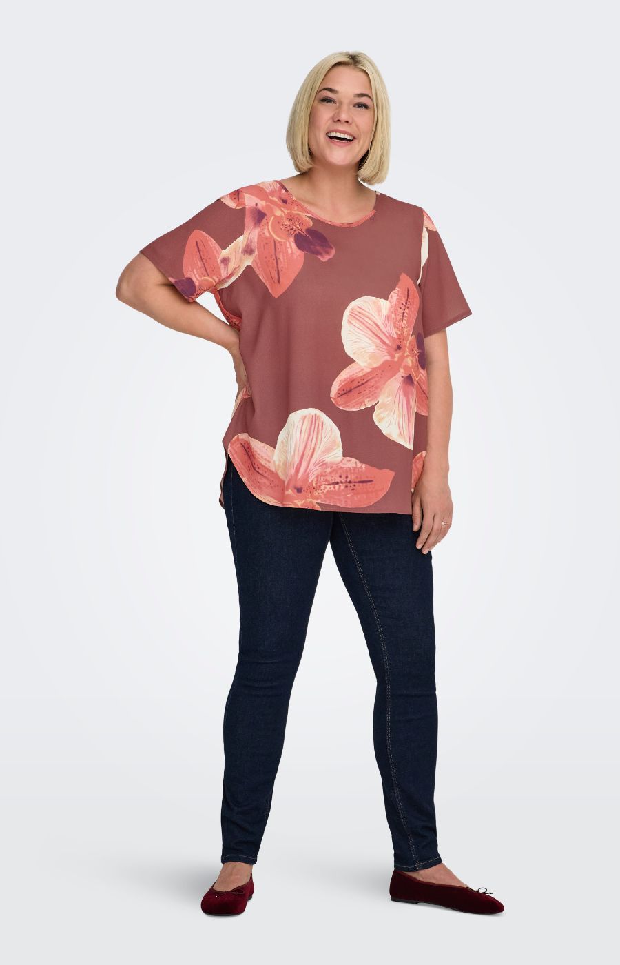 Woman wearing a rust colour, floral Vica blouse with dark jeans against a white background