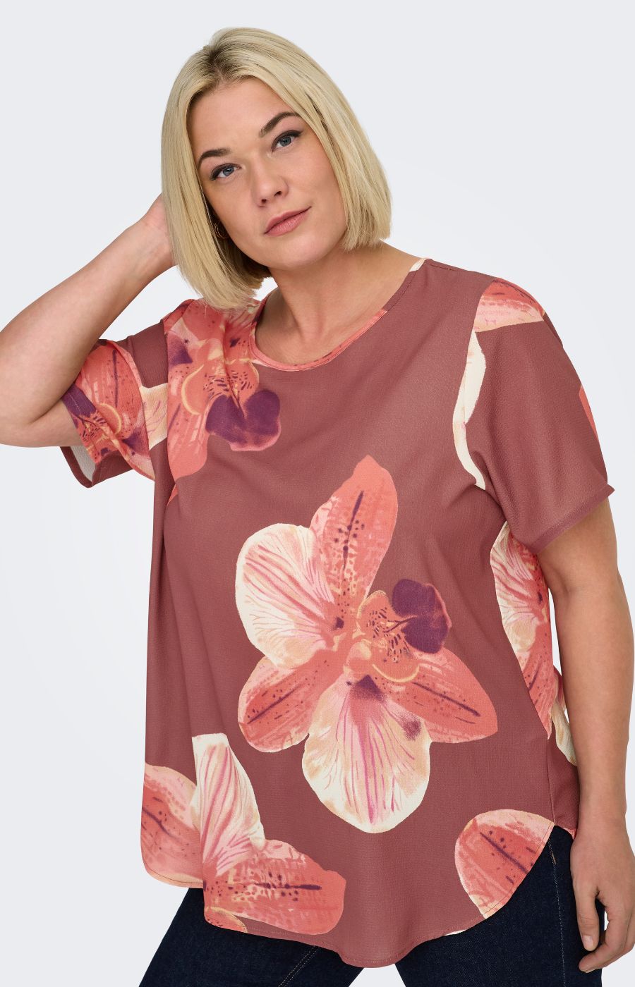 Woman wearing a rust colour, floral Vica blouse with dark jeans against a white background