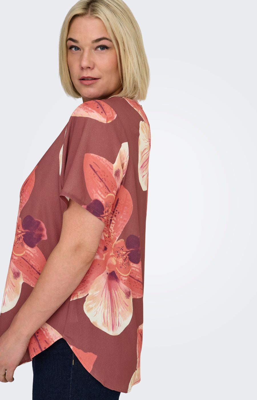 Woman wearing a rust colour, floral Vica blouse with dark jeans against a white background