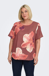 Woman wearing a rust colour, floral Vica blouse with dark jeans against a white background