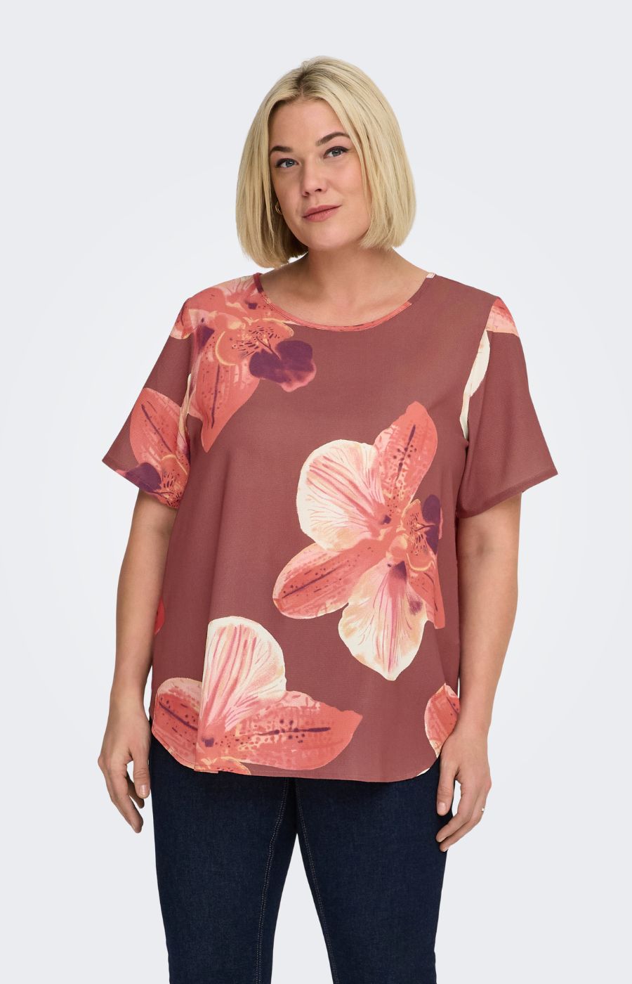 Woman wearing a rust colour, floral Vica blouse with dark jeans against a white background