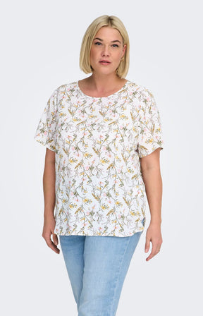 Woman wearing a white blouse, with a floral design all over and light blue jeans on a white background