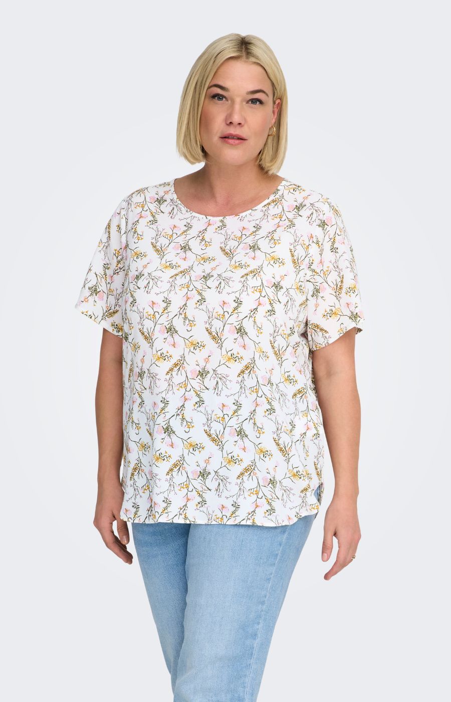 Woman wearing a white blouse, with a floral design all over and light blue jeans on a white background