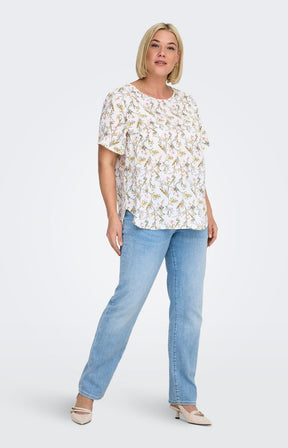 Woman wearing a white blouse, with a floral design all over and light blue jeans on a white background