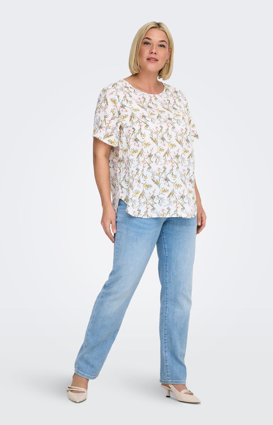 Woman wearing a white blouse, with a floral design all over and light blue jeans on a white background