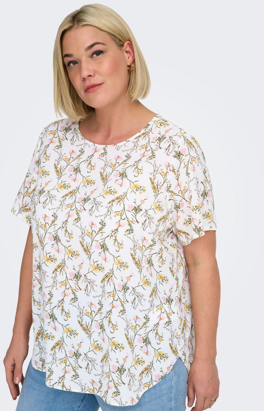 Woman wearing a white blouse, with a floral design all over and light blue jeans on a white background