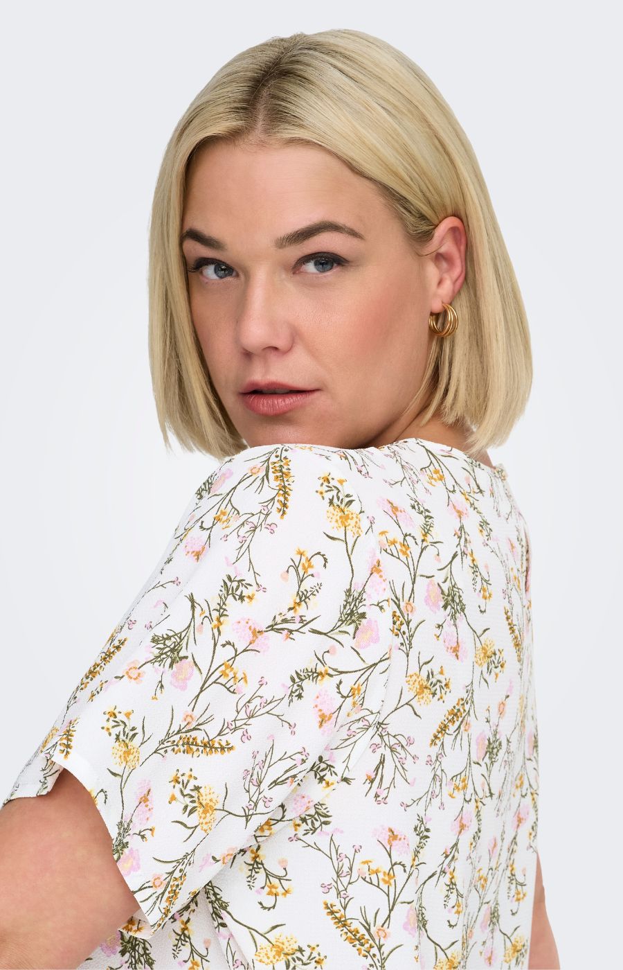 Woman wearing a white blouse, with a floral design all over against a white background 