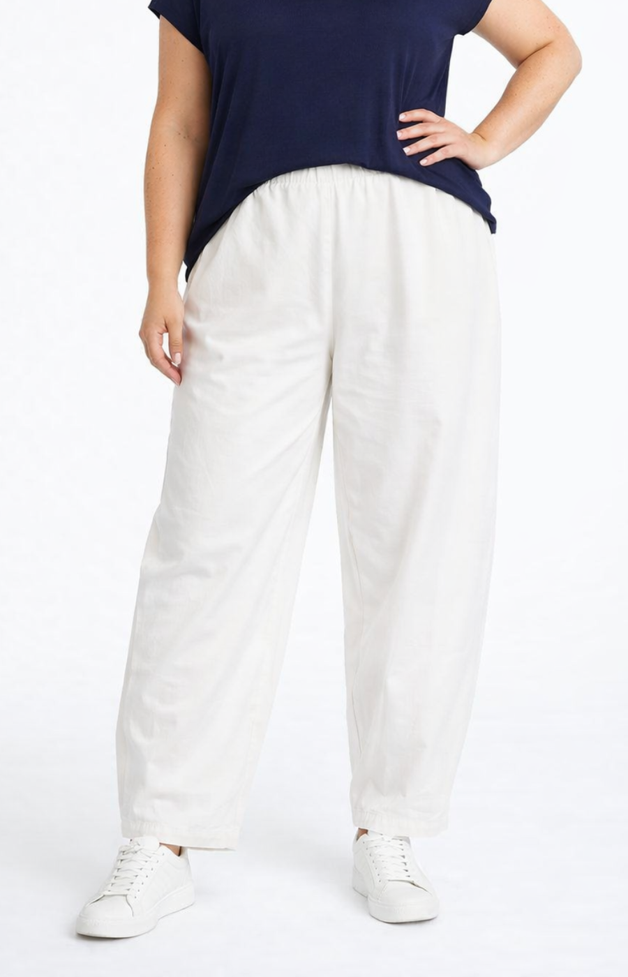 Person wearing a navy top and white pants on a white background