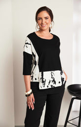 Woman wearing the Ora Contrasting Hem Top in Black, a black top with a contrasting side and hem with a round neckline, 1/2 length sleeves, cut out on the hem, pocket on the front with a plain background