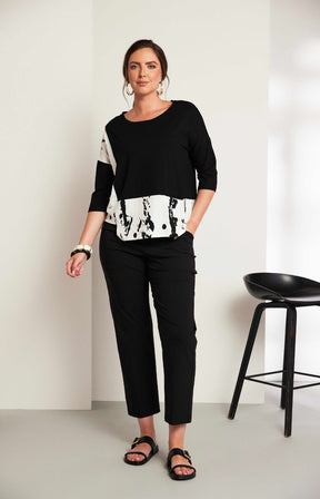 Woman wearing the Ora Contrasting Hem Top in Black, a black top with a contrasting side and hem with a round neckline, 1/2 length sleeves, cut out on the hem, pocket on the front with a plain background