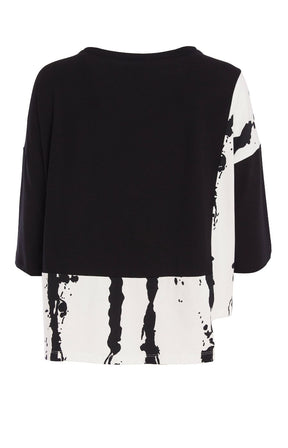 Woman wearing the Ora Contrasting Hem Top in Black, a black top with a contrasting side and hem with a round neckline, 1/2 length sleeves, cut out on the hem, pocket on the front with a plain background  