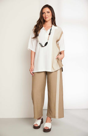 Woman wearing the Ora Crinkle Top with Collar in Beige, a white top with a beige side stripe down the front and back, a collard V neckline, short sleeves and side slits, worn with beige pants against a plain background 