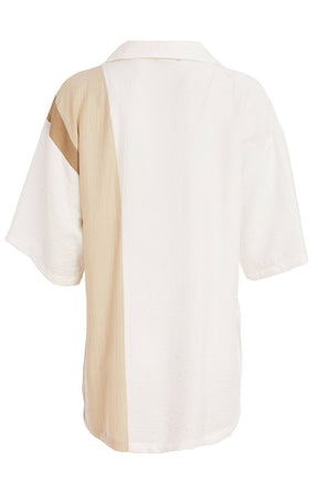 Woman wearing the Ora Crinkle Top with Collar in Beige, a white top with a beige side stripe down the front and back, a collard V neckline, short sleeves and side slits, worn with beige pants against a plain background  