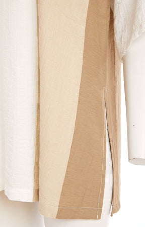 Woman wearing the Ora Crinkle Top with Collar in Beige, a white top with a beige side stripe down the front and back, a collard V neckline, short sleeves and side slits, worn with beige pants against a plain background   