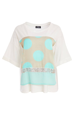 Woman wearing the Ora Dot T-Shirt with Turquoise, a lT-shirt with a round neckline and short sleeves  turquoise polka dots and sequin detailing and white trousers 