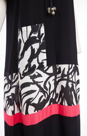 Woman wearing the Ora Dress in Black with Necklace, a black dress with a white, black and pink  design on the fron, front pocket, short sleeves and a round neckline against a white background 